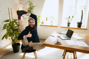 Dehnen. Junger, flexibler bärtiger Mann, Bürokaufmann, der Spaß hat und Yoga auf einem Holztisch im modernen Büro während der Arbeitszeit mit Gadgets macht. Konzept von Geschäft, gesundem Lebensstil, Sport, Hobby