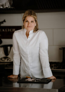 Annette Glücklich in einer weißen Kochjacke in ihrer Küche vor der Arbeitsplatze