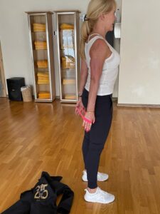 Blonde Frau führt eine Übung mit einem Theraband durch in einem Übungsraum für bessere Bewegung 